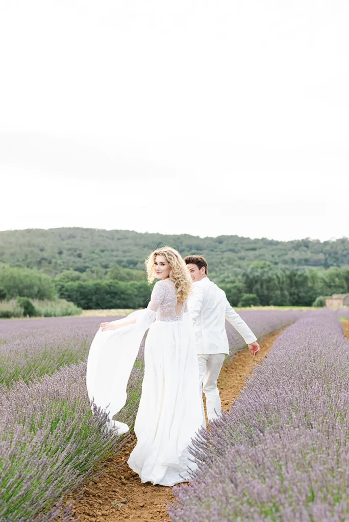 Couple de mariés marchant dans les champs de lavandes après leurs mariage à la Chartreuse de Valbonne en provence